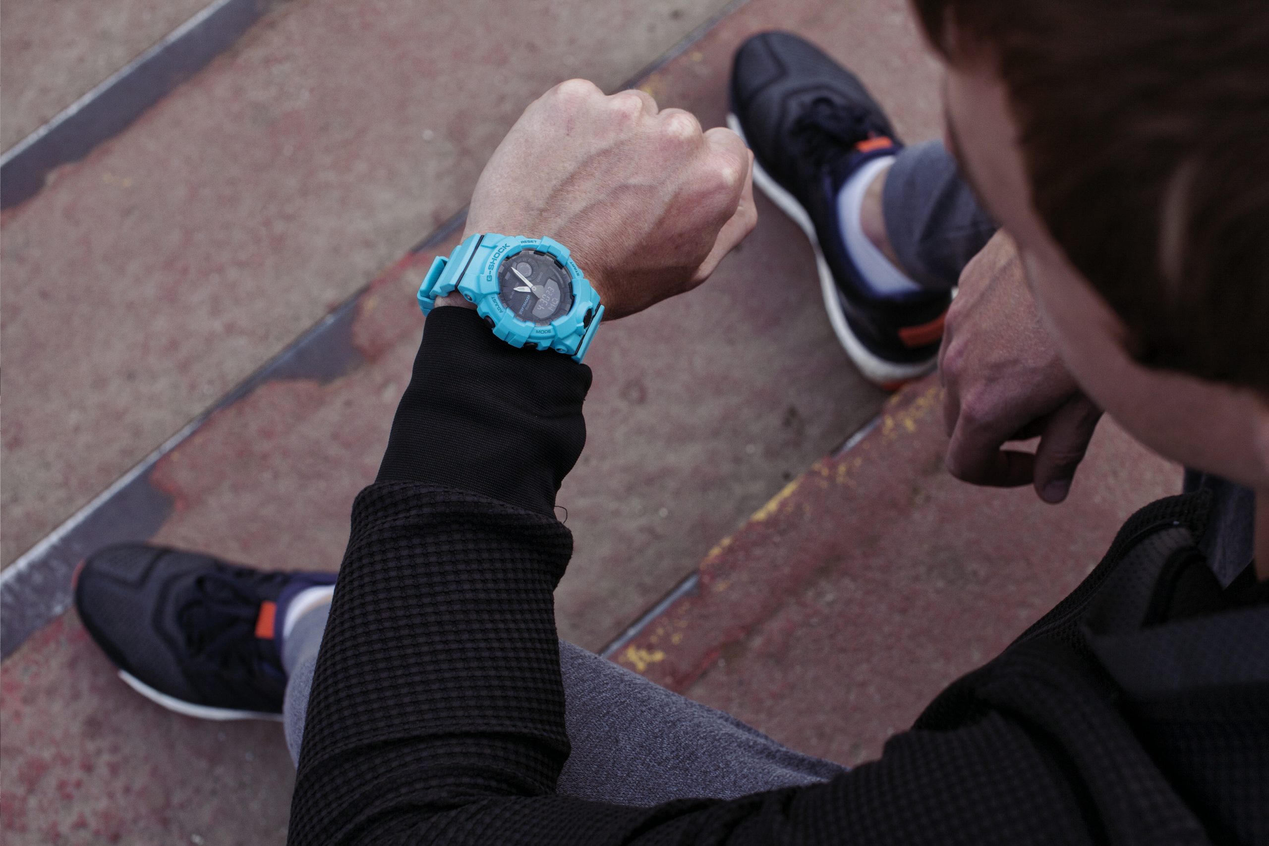 siedzący mężczyzna, który spogląda na zegarek G-SHOCK GBA-800 w kolorze niebieskim