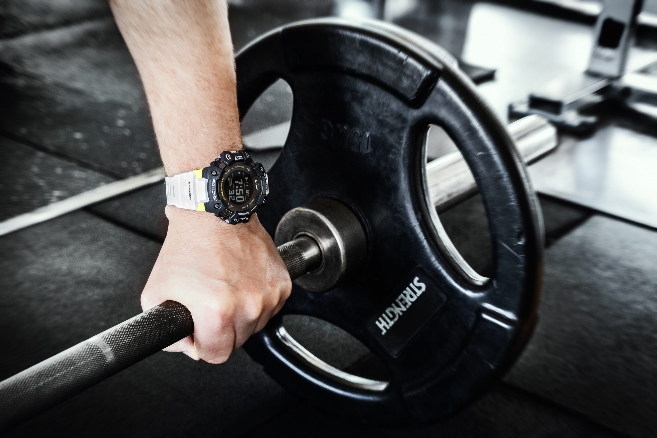 Męska ręka sięgająca po sztangę, na nadgarstku widnieje zegarek GBD-H1000